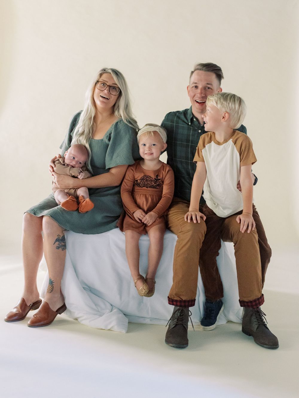 A family of five sits together for a studio portrait against a light beige background.