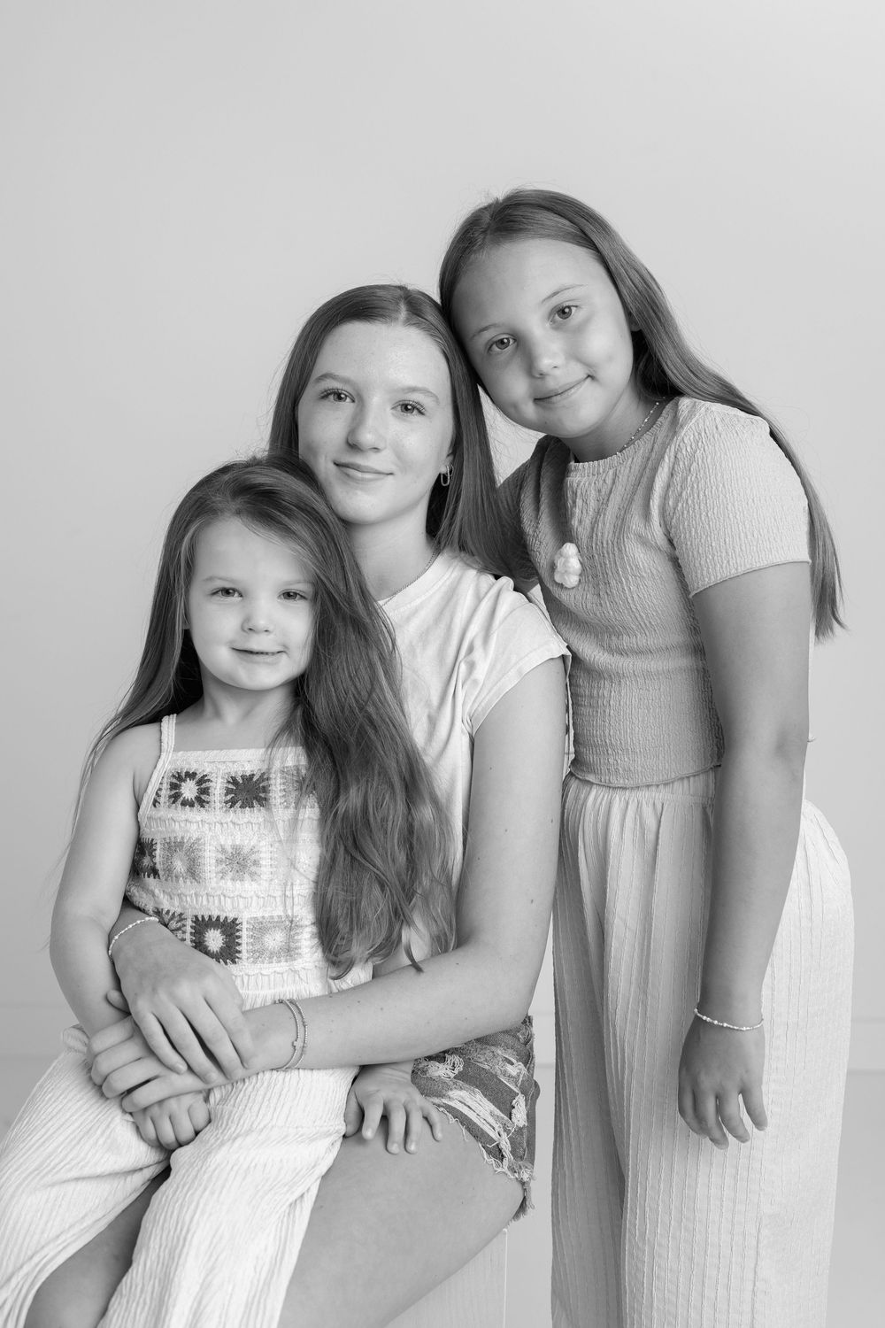 Three young girls in casual attire posing together for a black and white portrait.