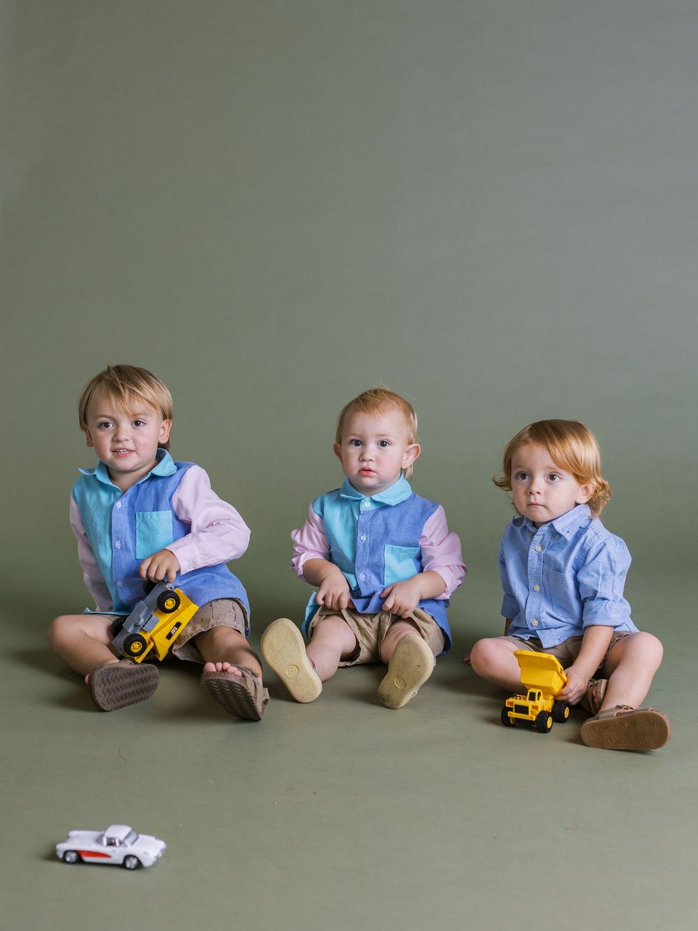 A series of milestone progression photos showing babies sitting with toy cars on a neutral gray backdrop.