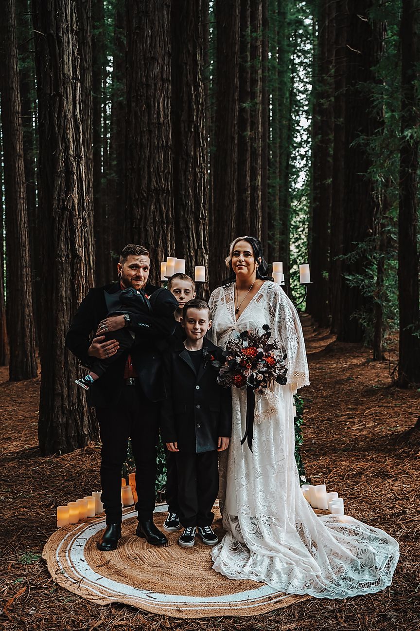 A wedding party poses in a majestic redwood forest with a long flowing white dress train spread across the ground.