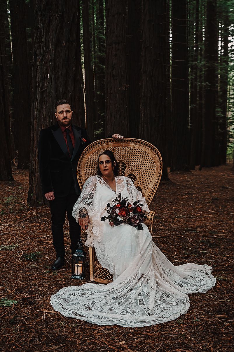 A beautiful forest wedding photoshoot with vintage decor featuring a wicker peacock chair and flowing lace dress.