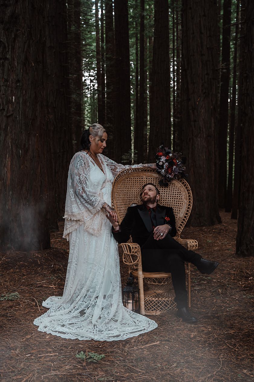 Romantic forest wedding photography featuring a rattan peacock chair and delicate white lace gown against towering trees.