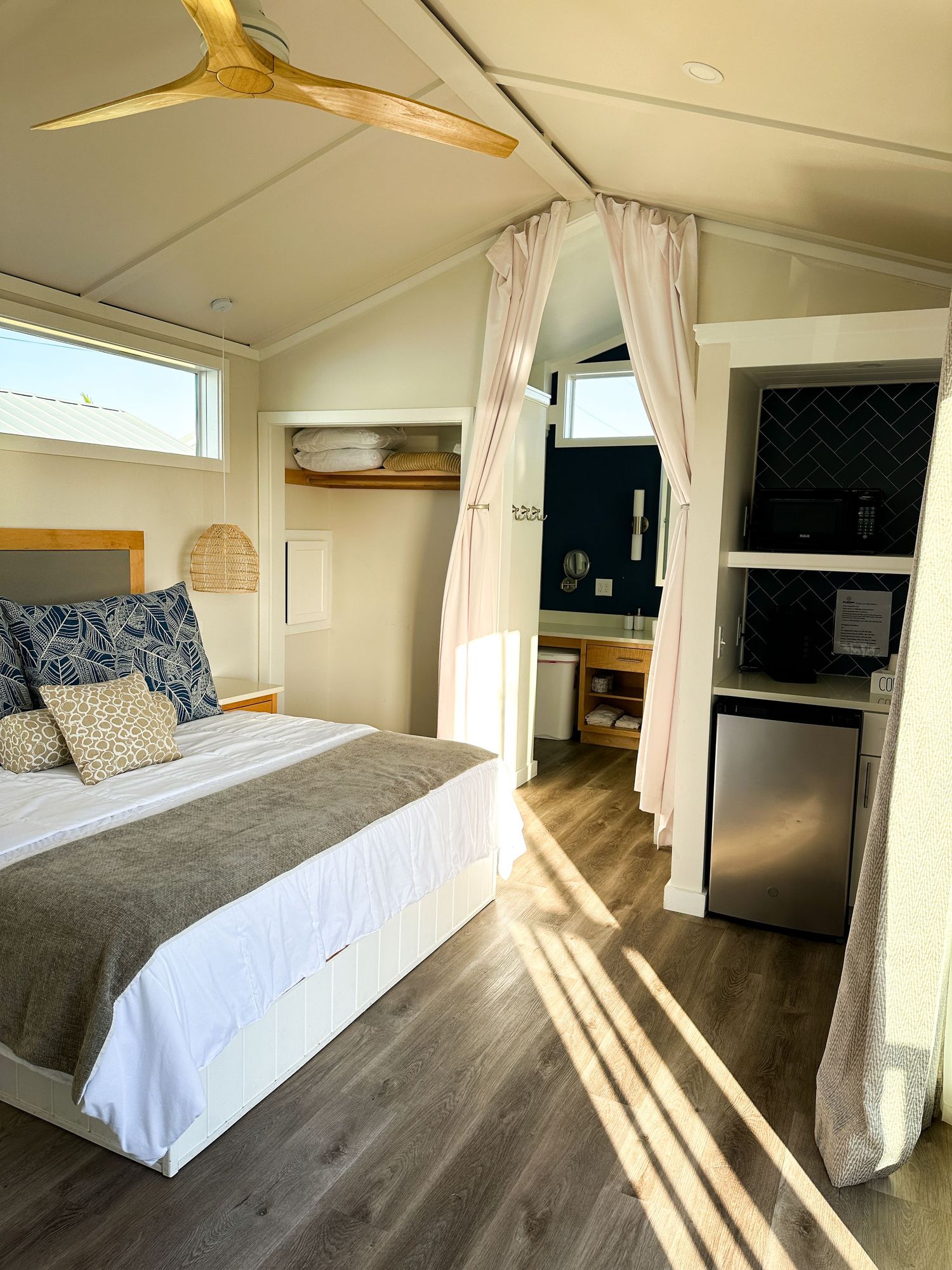 Bright modern glamping cabin interior with queen bed, ceiling fan, and kitchenette.