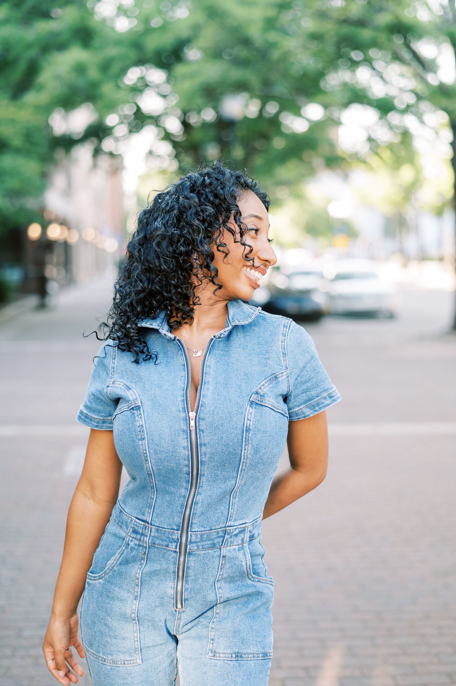 Short sleeve denim romper with zipper front shown in casual lifestyle photos against blurred outdoor background in Fayetteville NC
