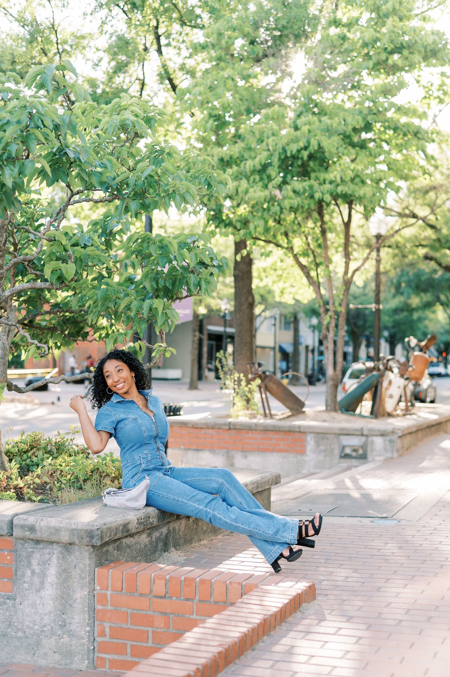 Someone in a denim jumpsuit poses playfully on brick walls and benches in a tree-lined and backlit downtown Fayetteville NC