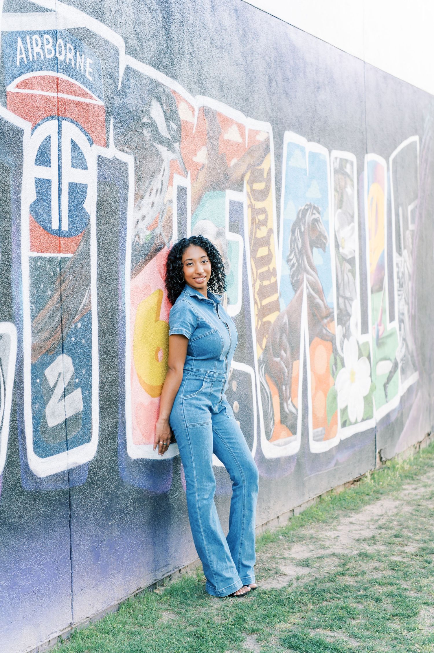 Woman in denim jumpsuit posing against colorful graffiti wall in downtown Fayetteville NC.