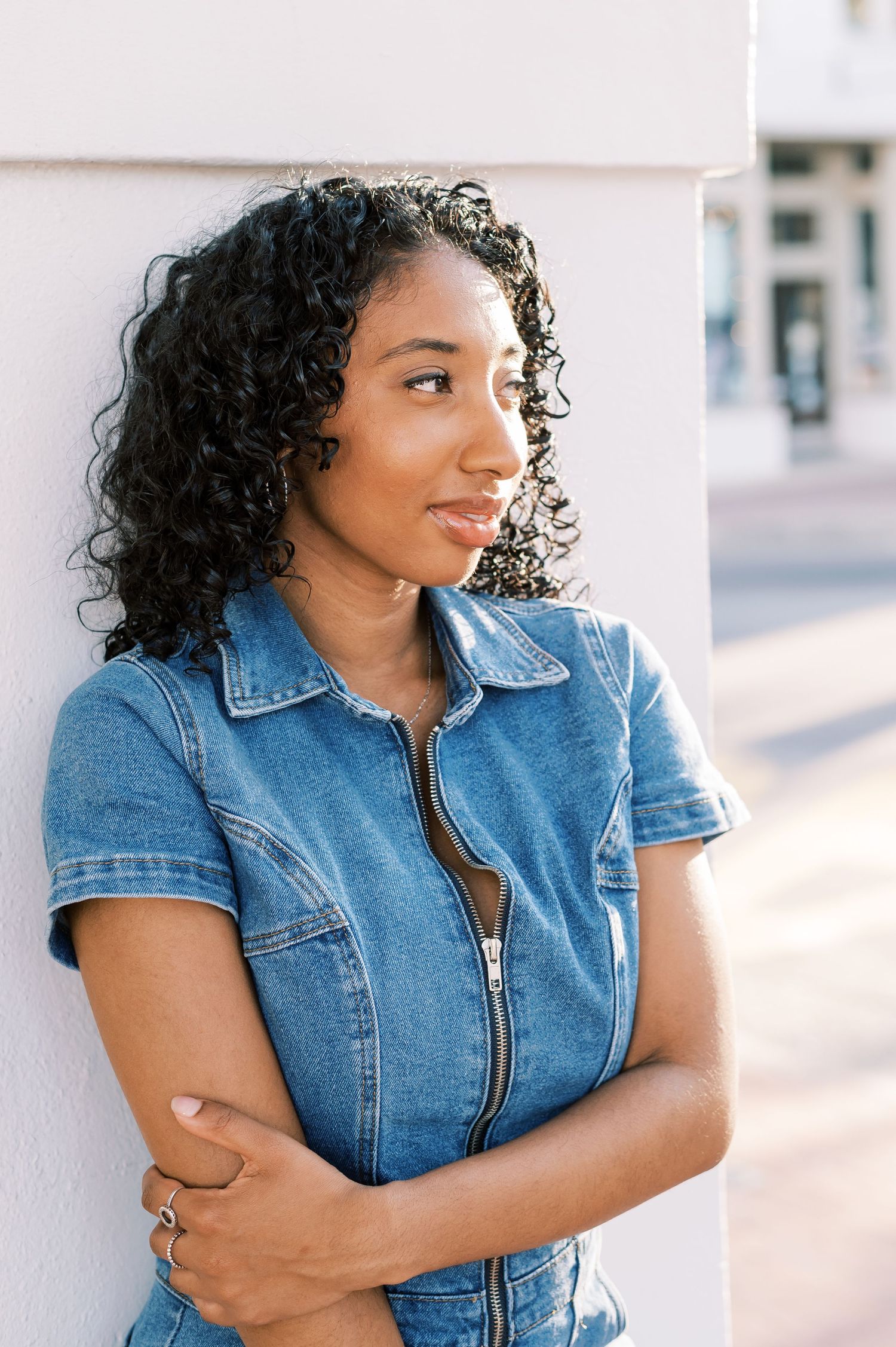 Woman in denim jumpsuit posing against light colored wall in downtown Fayetteville NC.