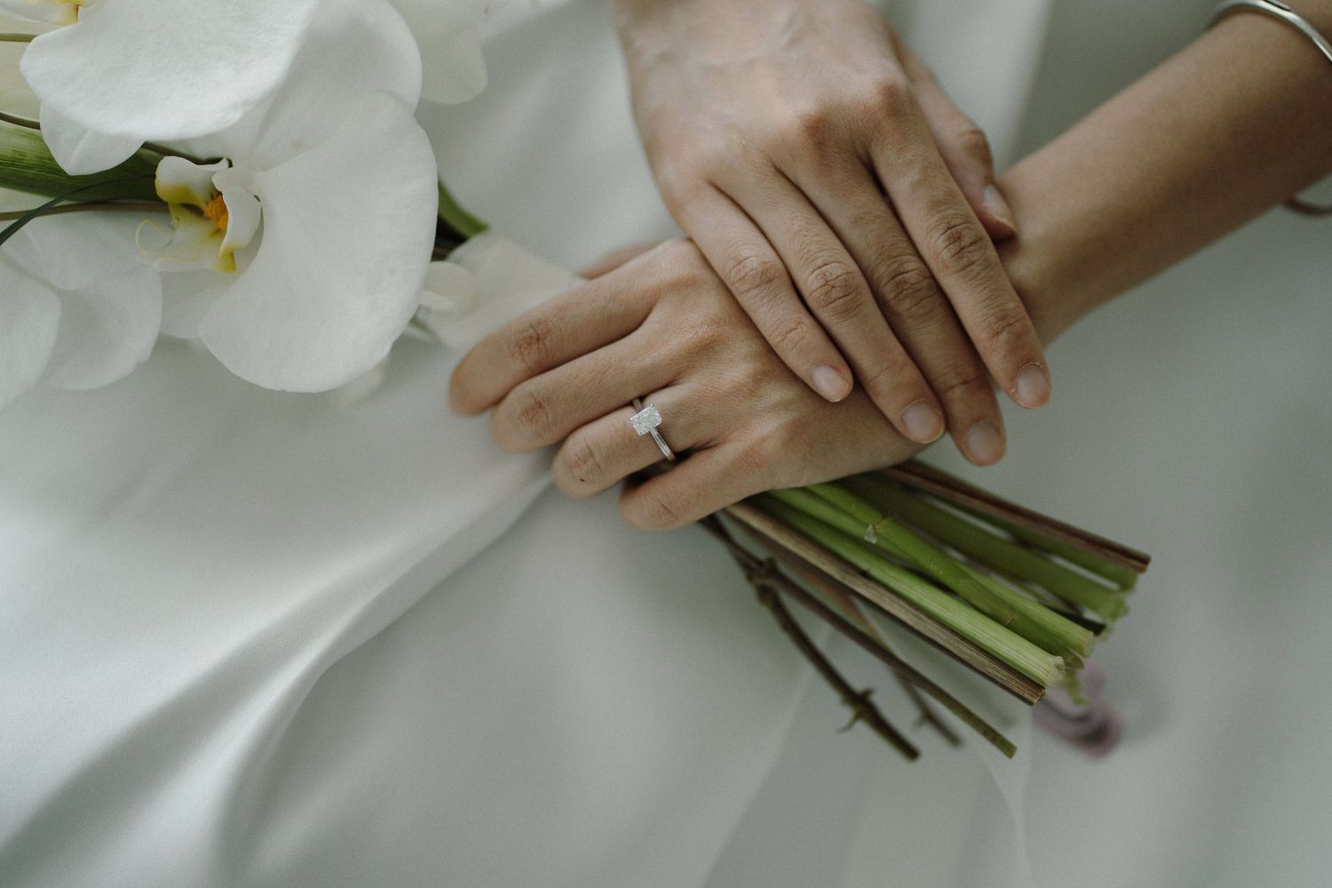 Close-up of hands holding white orchid wedding bouquet with engagement ring.