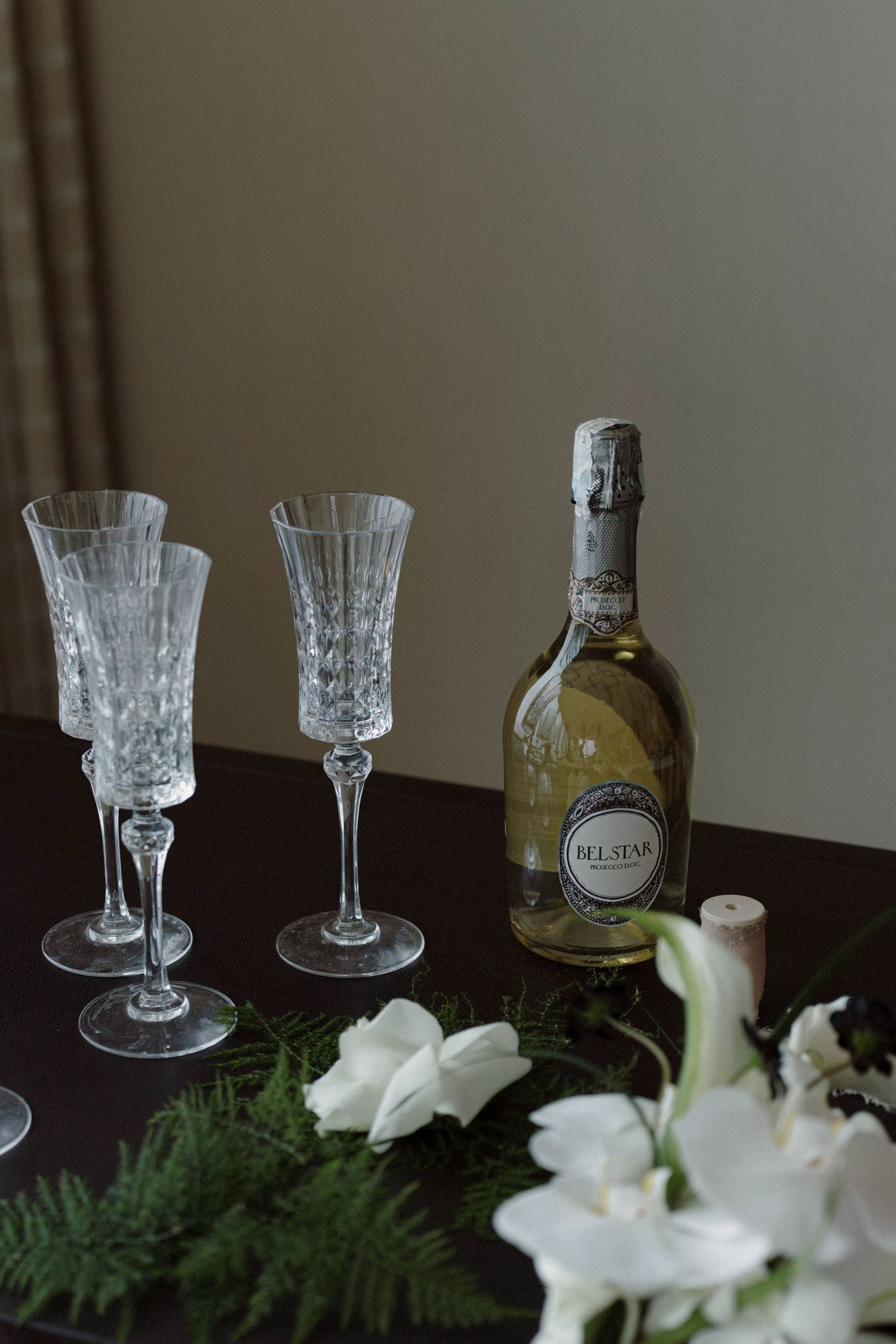 Crystal glassware and white wine bottle arranged with white floral decorations.