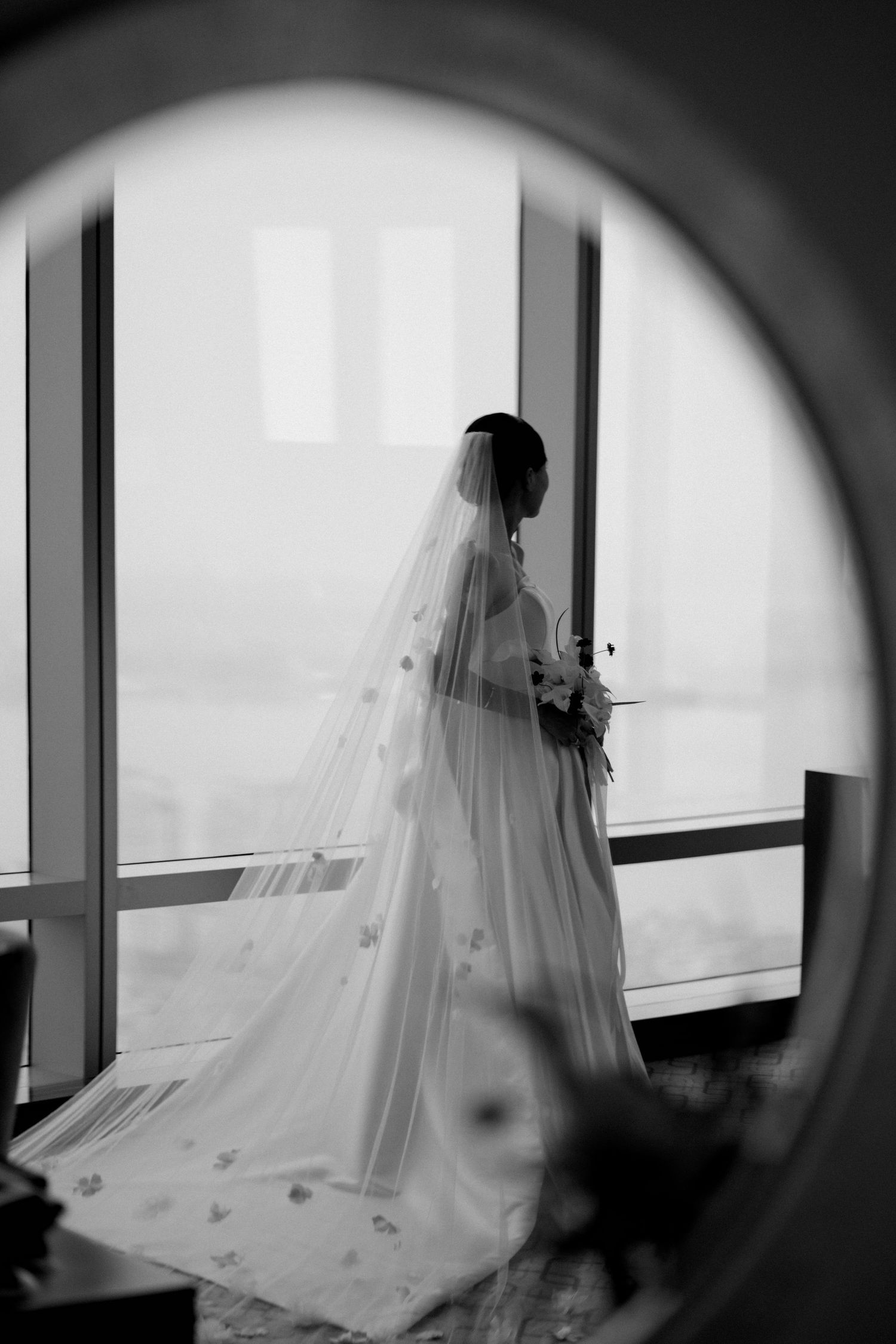 Silhouette of a bride through a circular window frame in dramatic black and white.