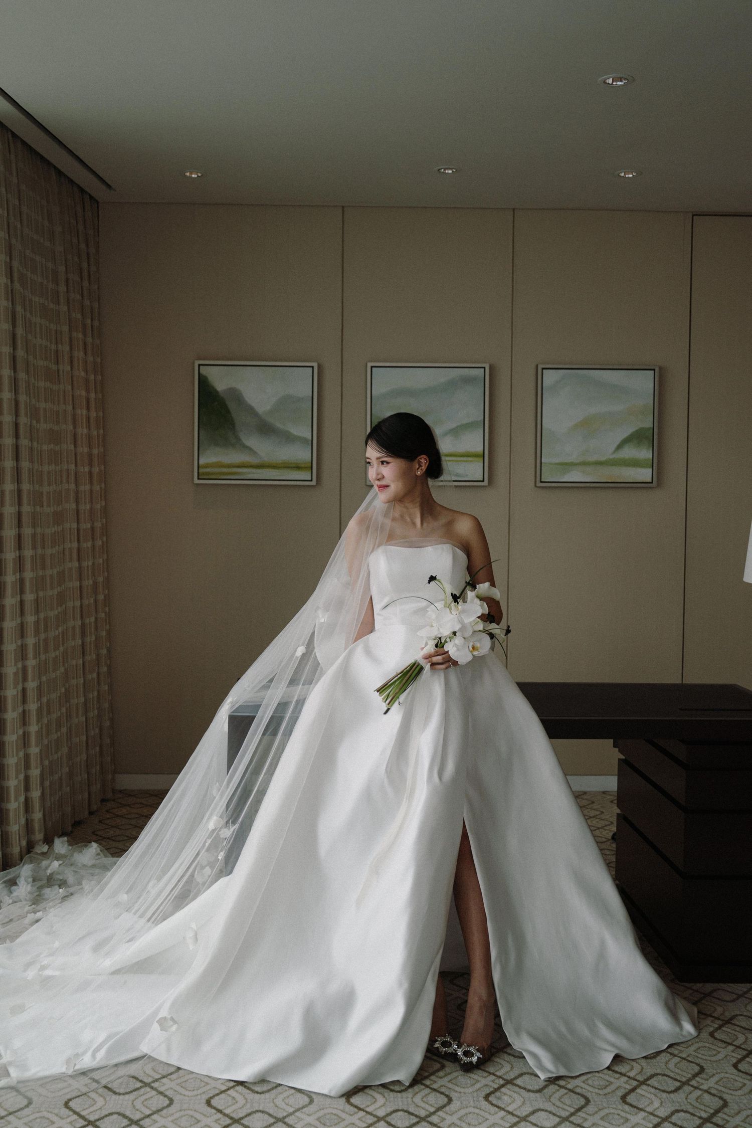 Elegant white wedding gown with long train displayed in a luxurious hotel room.