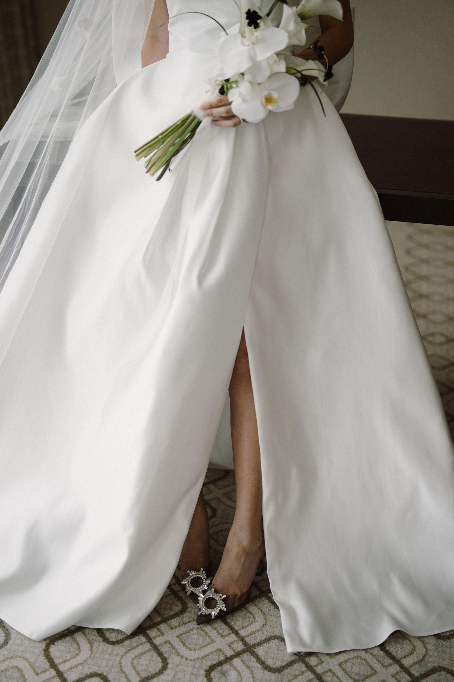 Close-up details of a white wedding dress and bouquet against a patterned carpet.
