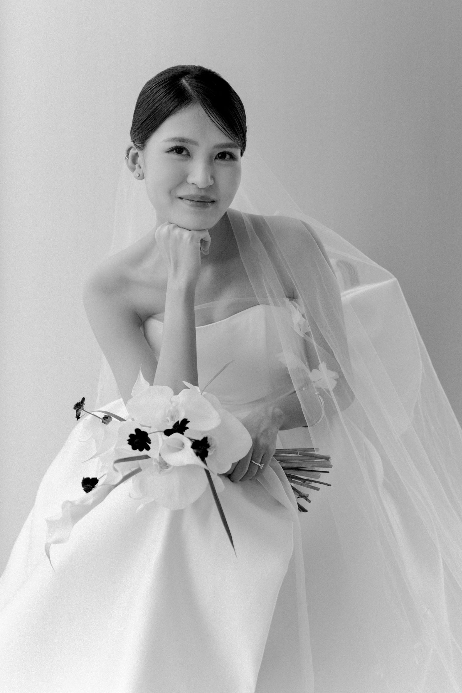 Minimalist bridal portrait with white orchid bouquet and flowing veil.