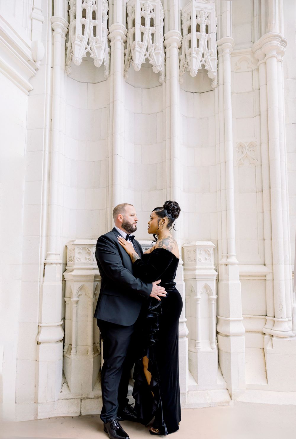A couple shares an intimate moment against ornate white gothic architecture pillars.