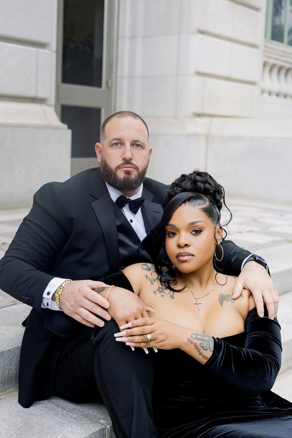 Couple in formal black attire poses intimately on marble steps for artistic wedding photography.