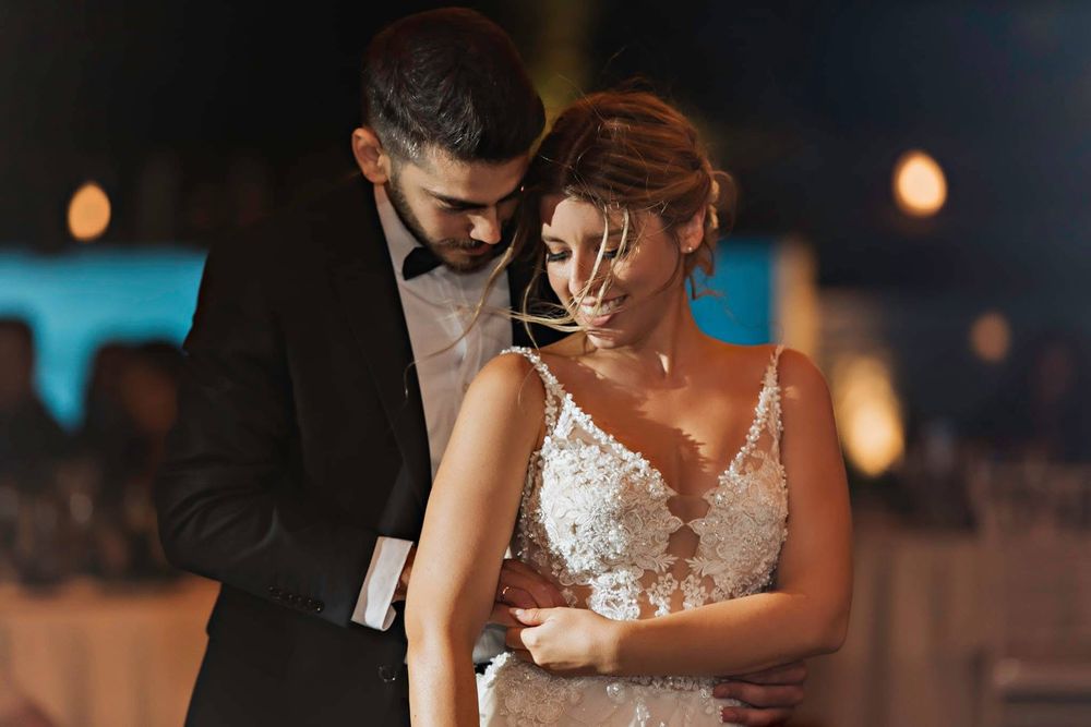 A couple shares an intimate moment during their first dance at an evening wedding reception with glowing lights.