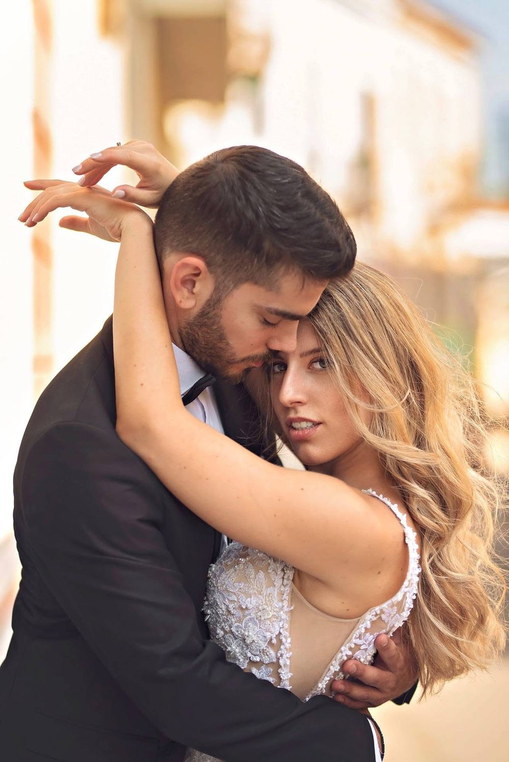 Romantic wedding couple dancing and embracing in golden sunlight against an urban backdrop.