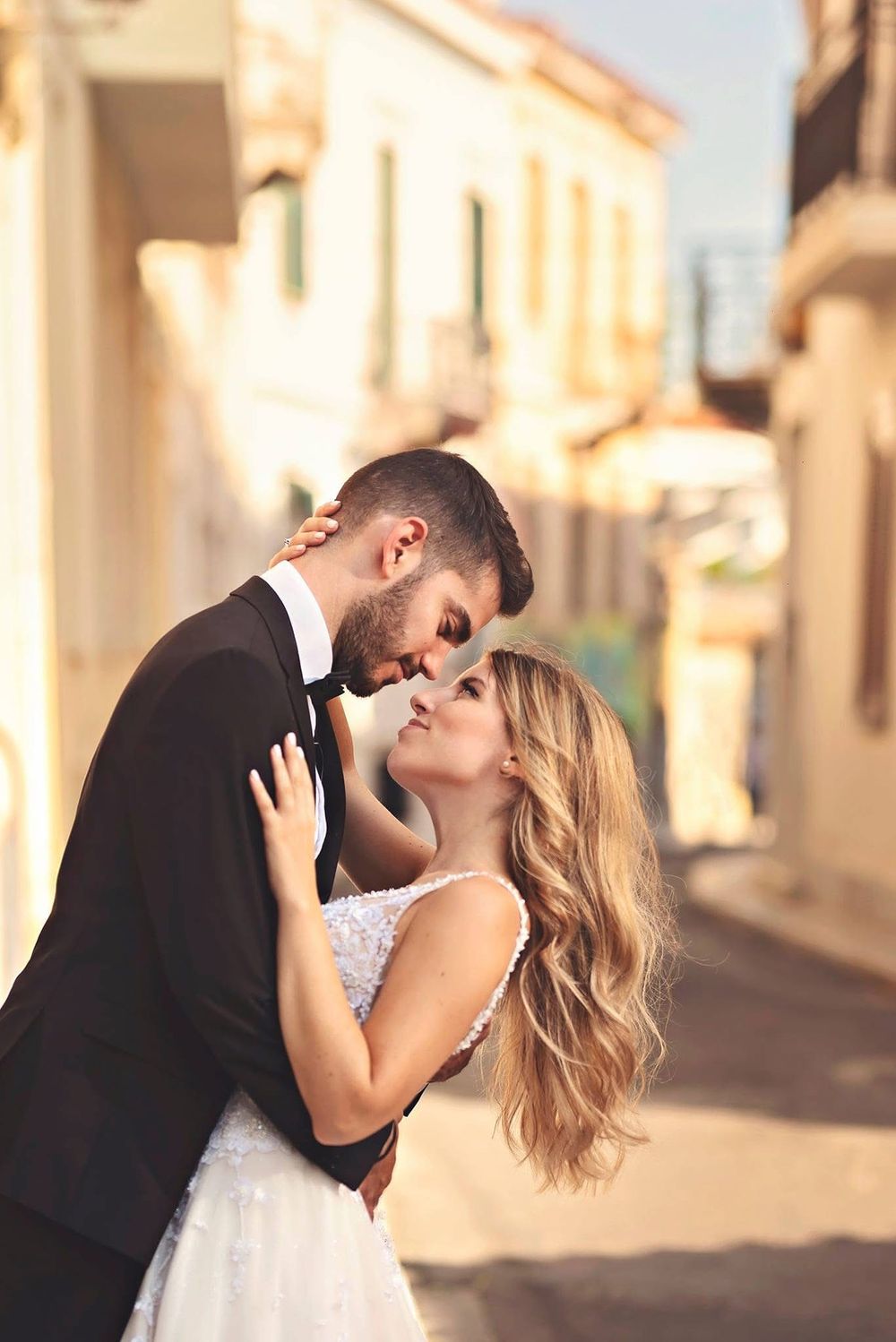 A romantic bride and groom share multiple passionate kisses during their wedding photoshoot on a sunlit European street.