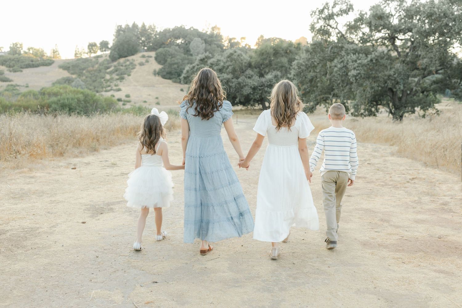 A group walking together along a dirt path through golden hills at sunset while holding hands captured by Chelsee Rawe Photography.