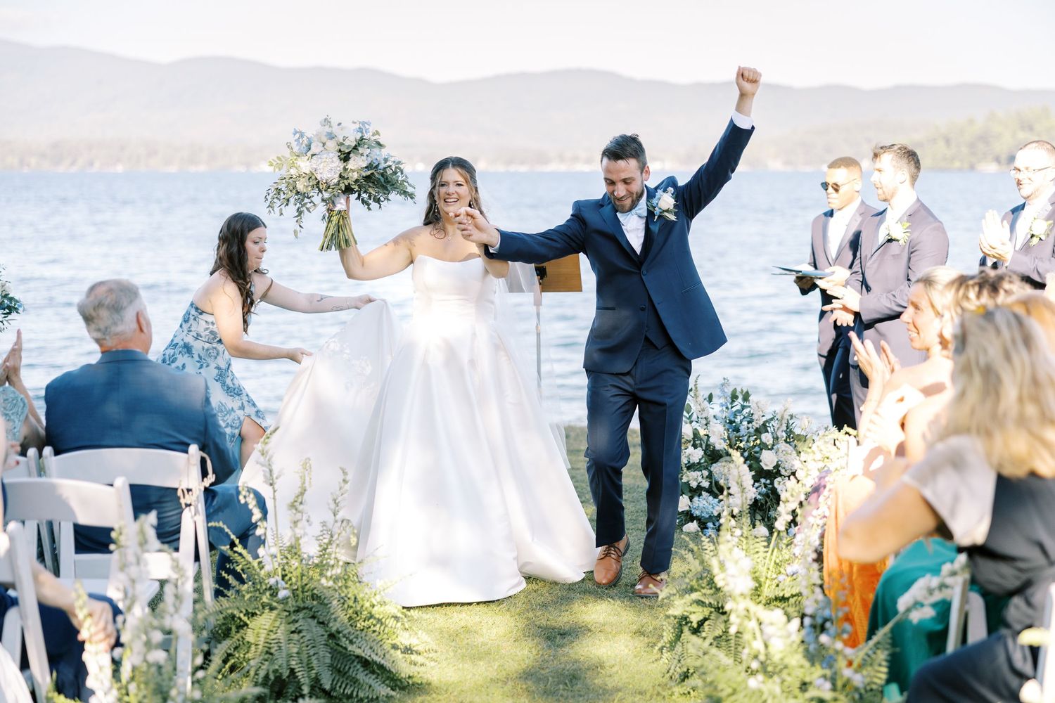 A happy couple celebrates at their outdoor lakeside wedding ceremony surrounded by guests and natural scenery.