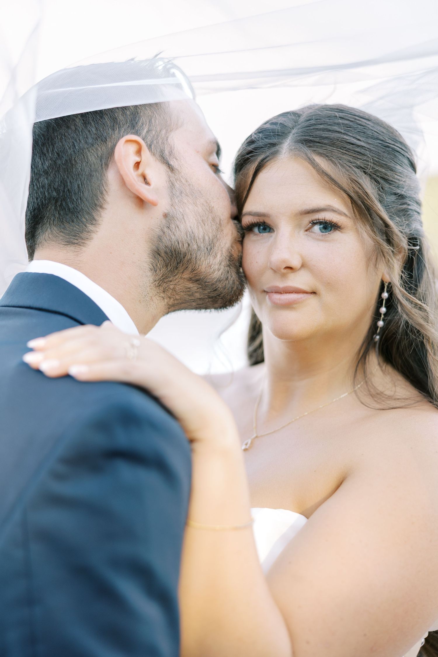 A romantic series of wedding photos showing intimate moments between newlyweds under a white veil during their photoshoot.