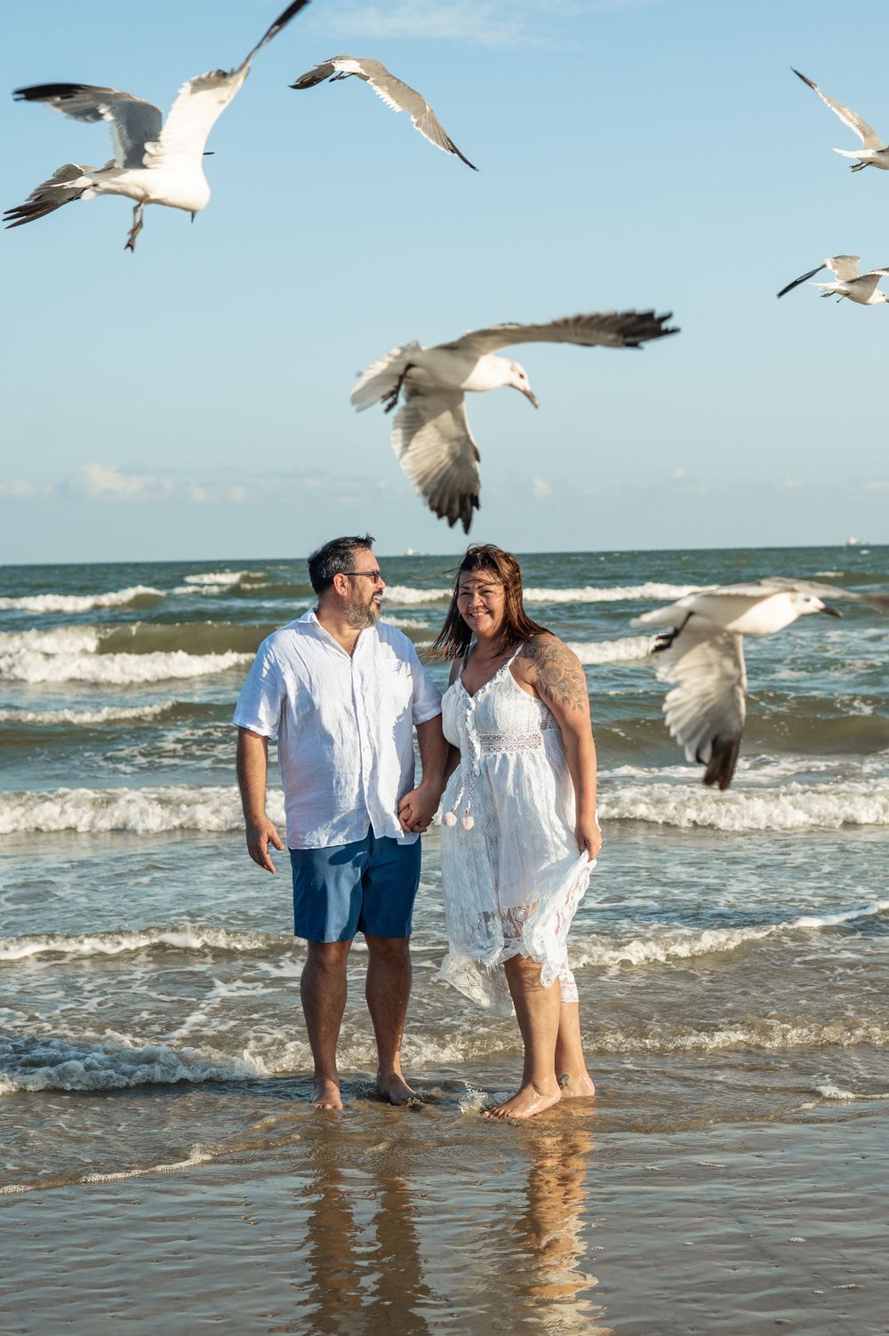 People enjoying a beach walk while seagulls fly overhead on a sunny summer day.