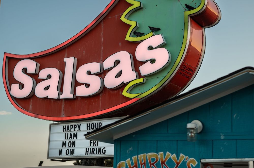 Colorful retro-style restaurant signage with neon lights displaying menu items against a teal-colored exterior wall.