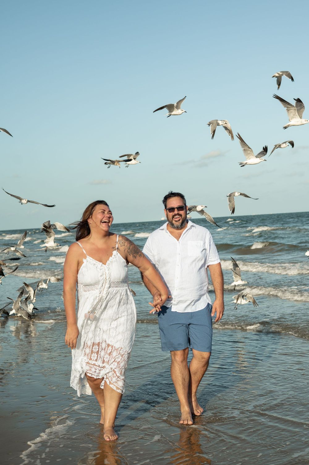 People wading in ocean water with seagulls flying around them against a bright blue sky.