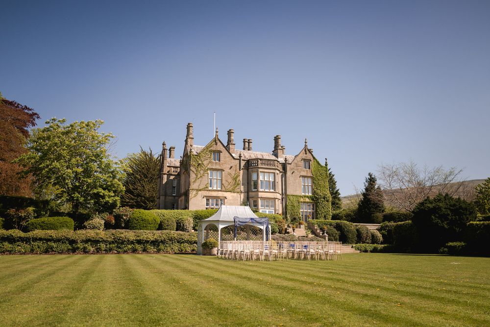 Panoramic exterior view of a grand country estate mansion with manicured lawns and gardens.