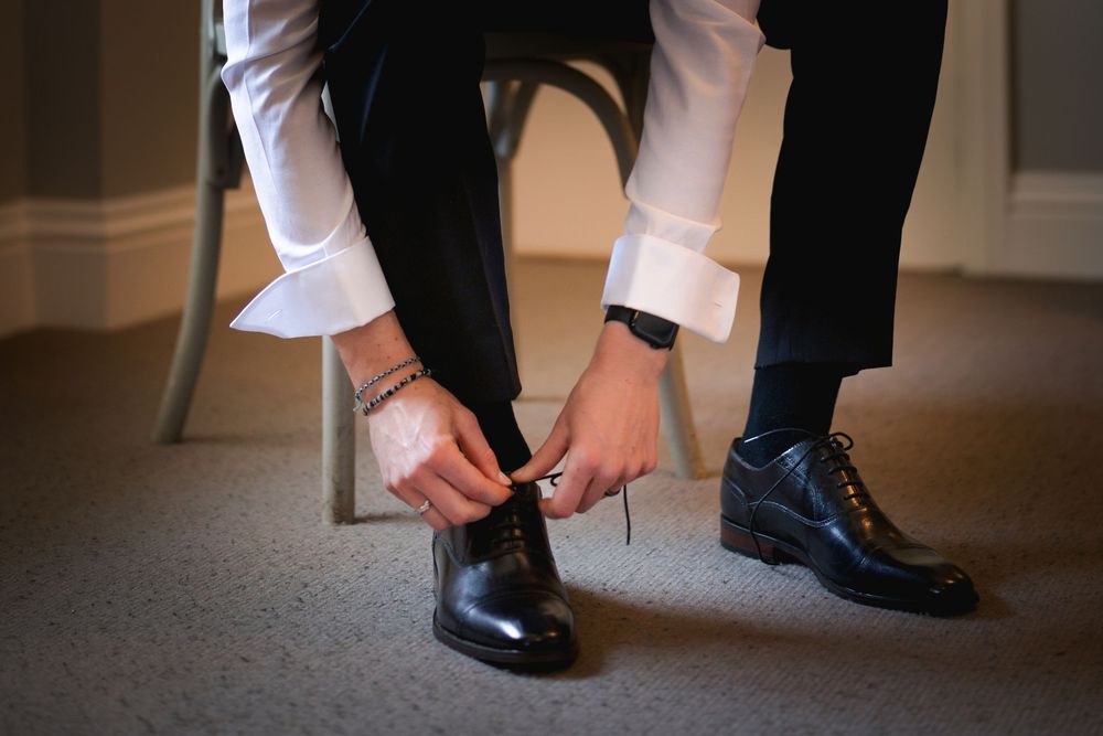 Close-up of polished black dress shoes and formal attire at a wedding event.