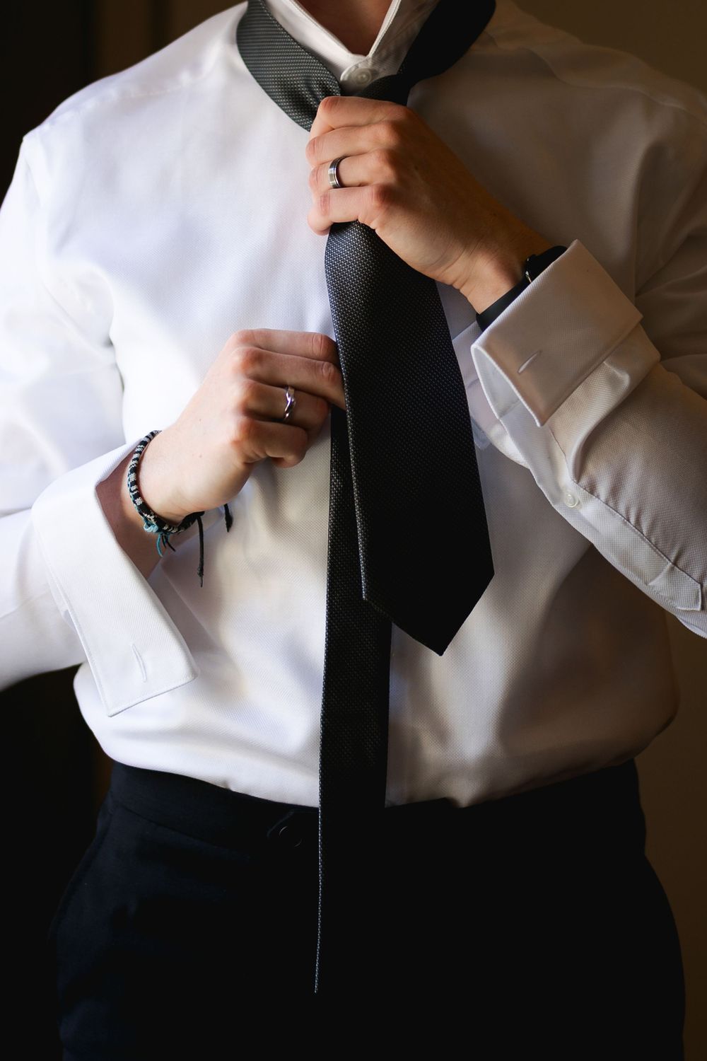 Detail shot of hands adjusting a black tie against a crisp white dress shirt.