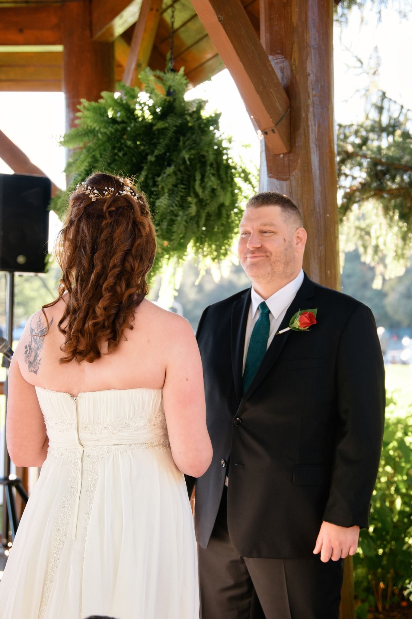 A tender moment between a bride and groom sharing laughs during an outdoor wedding ceremony under a wooden gazebo.