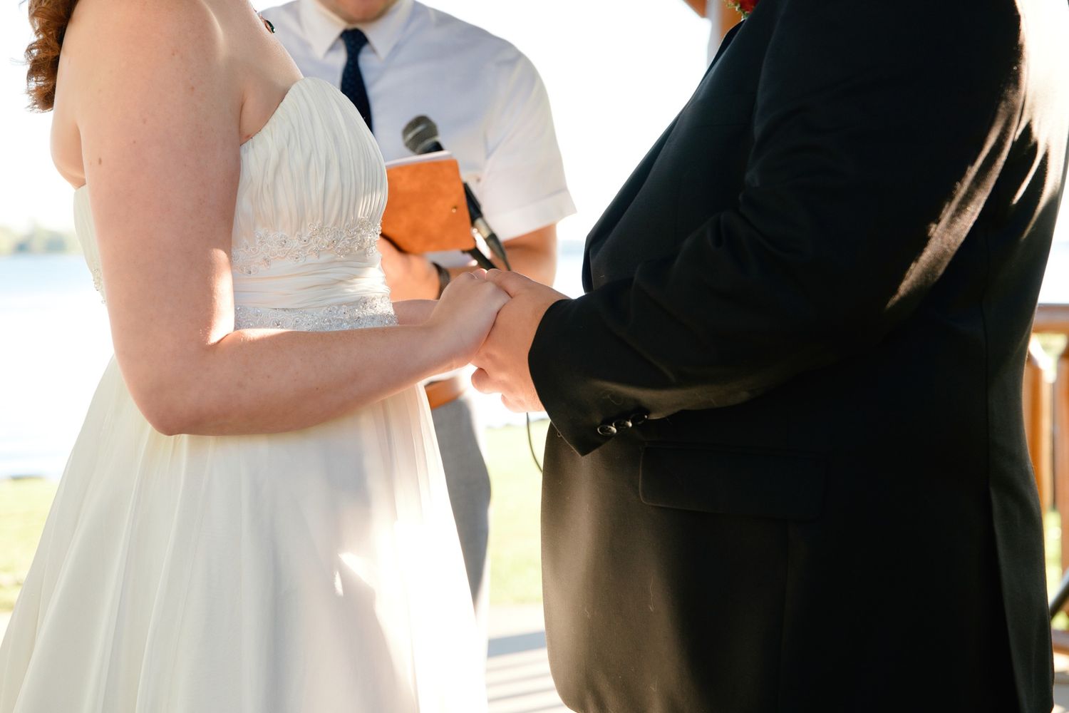 Close up of hands during a wedding ceremony with white dress fabric and dark suit visible.