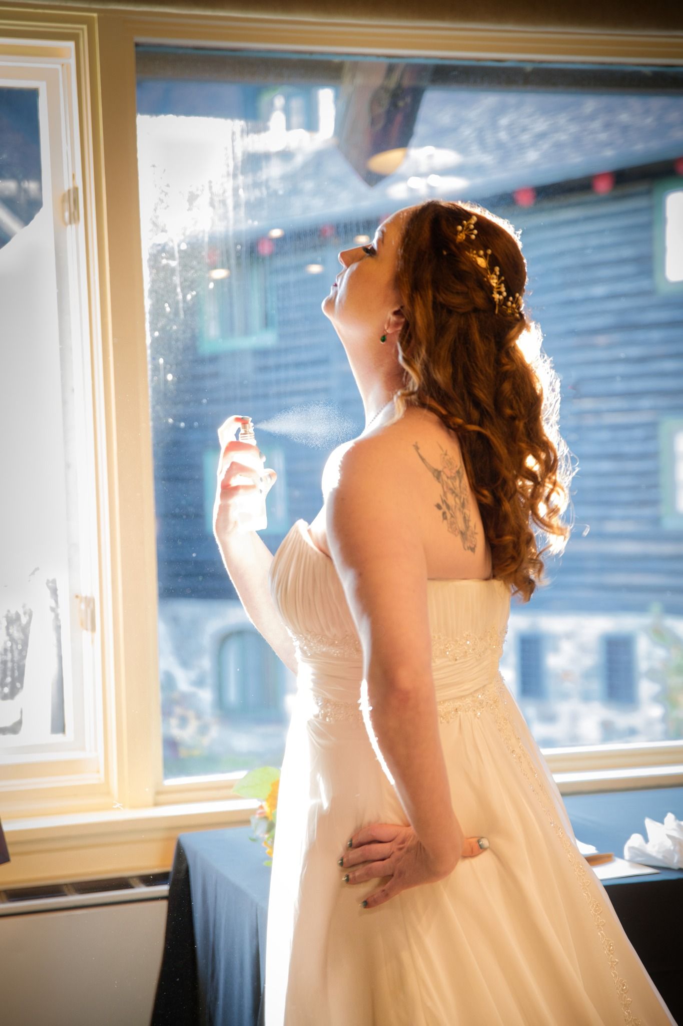 Bride in white dress poses by sunlit windows during wedding preparation.