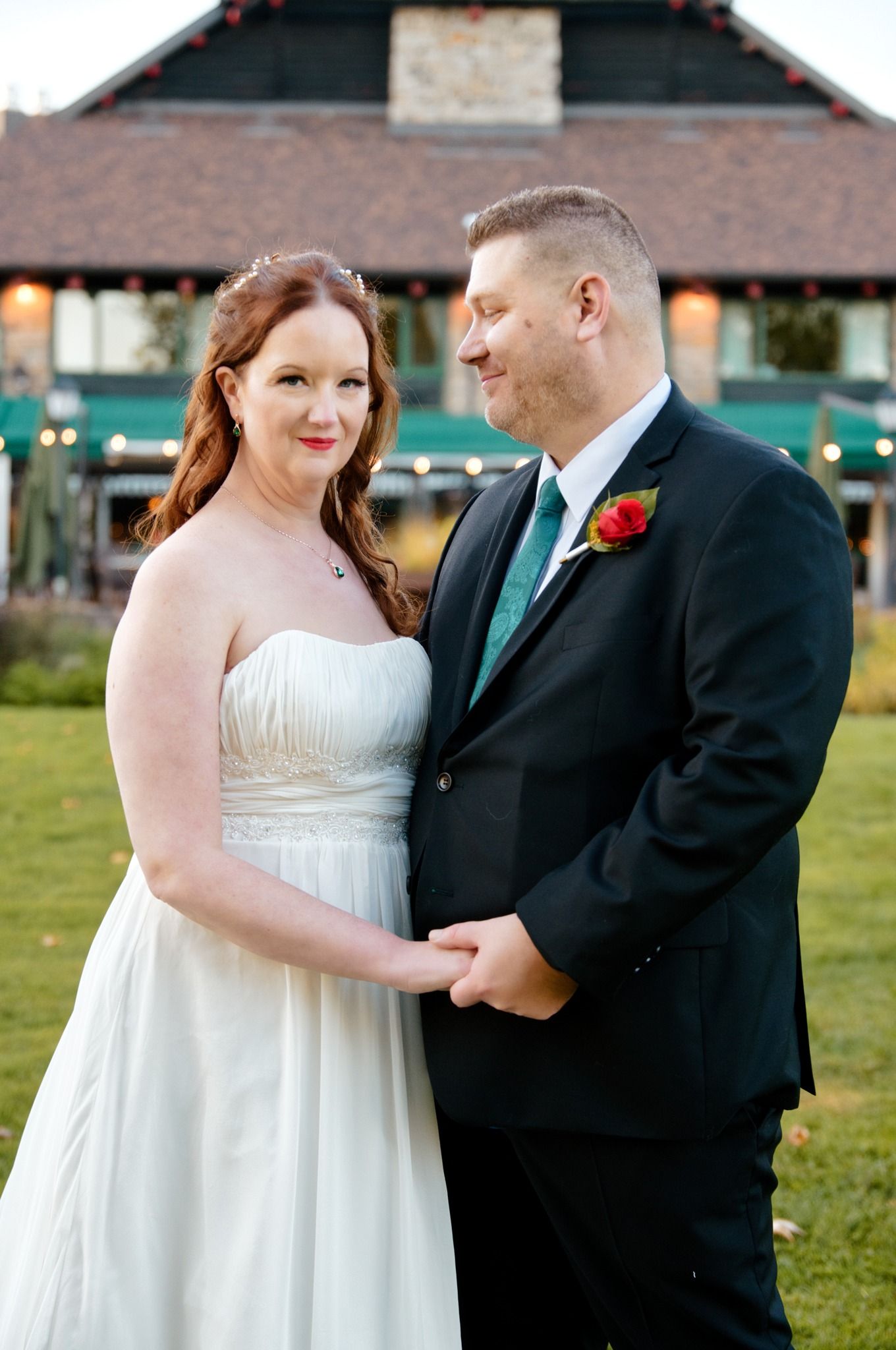 Couple shares intimate outdoor moment in white dress and black suit with red boutonniere.