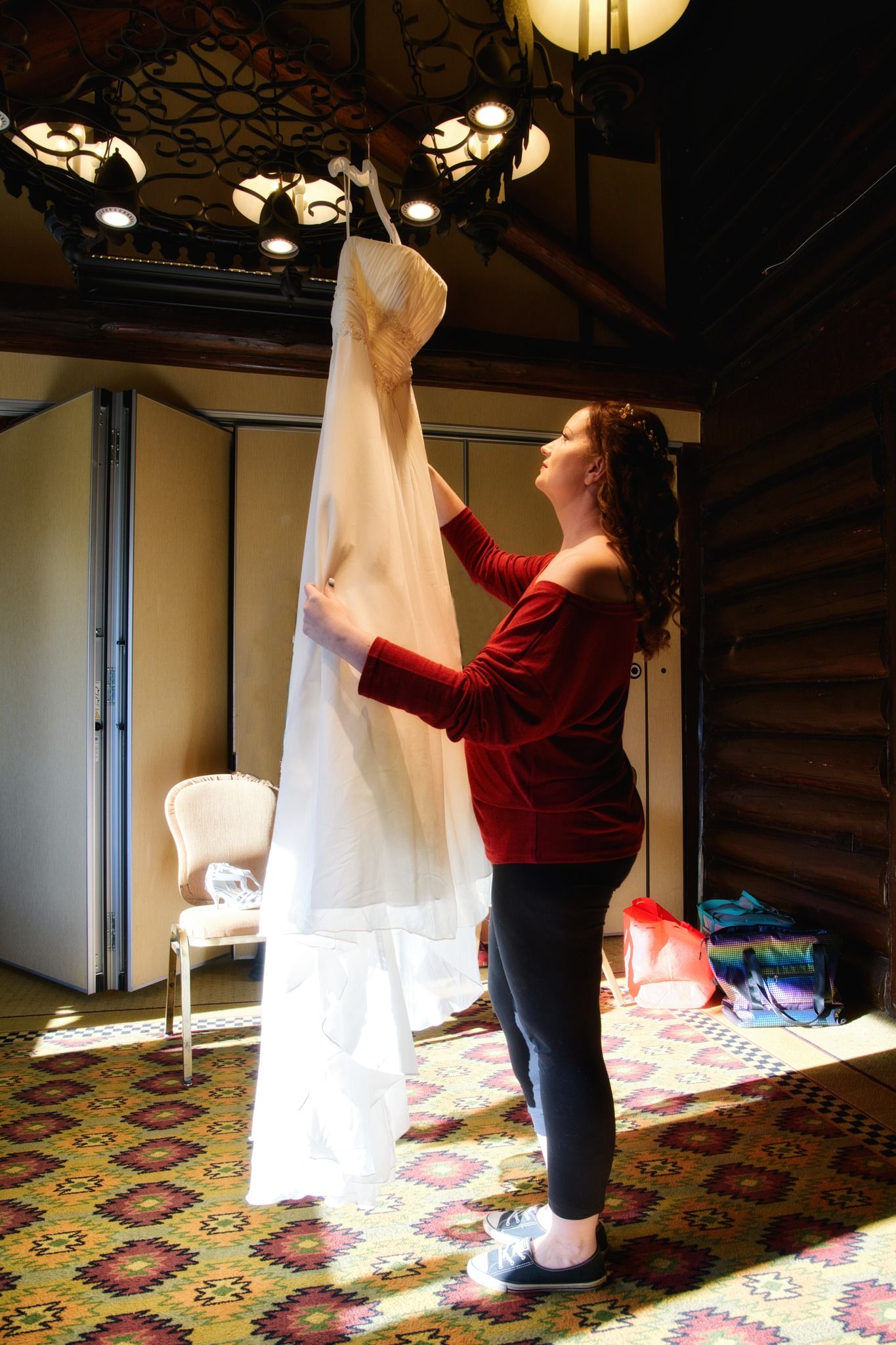 Someone in a red sweater examines a long white bridal veil against the sunlight filtering through ornate windows.