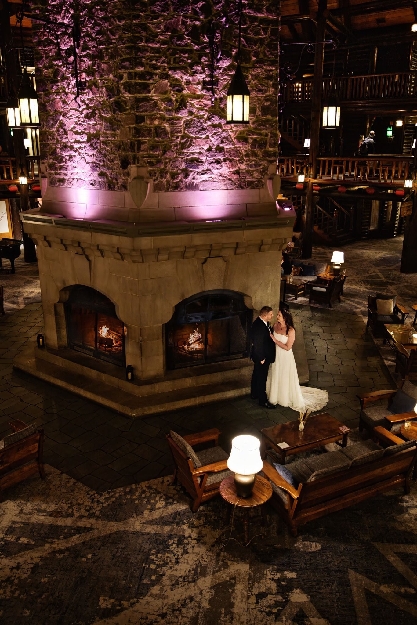 A white dress twirls against a rustic stone wall backdrop illuminated with purple uplighting in an intimate venue setting.