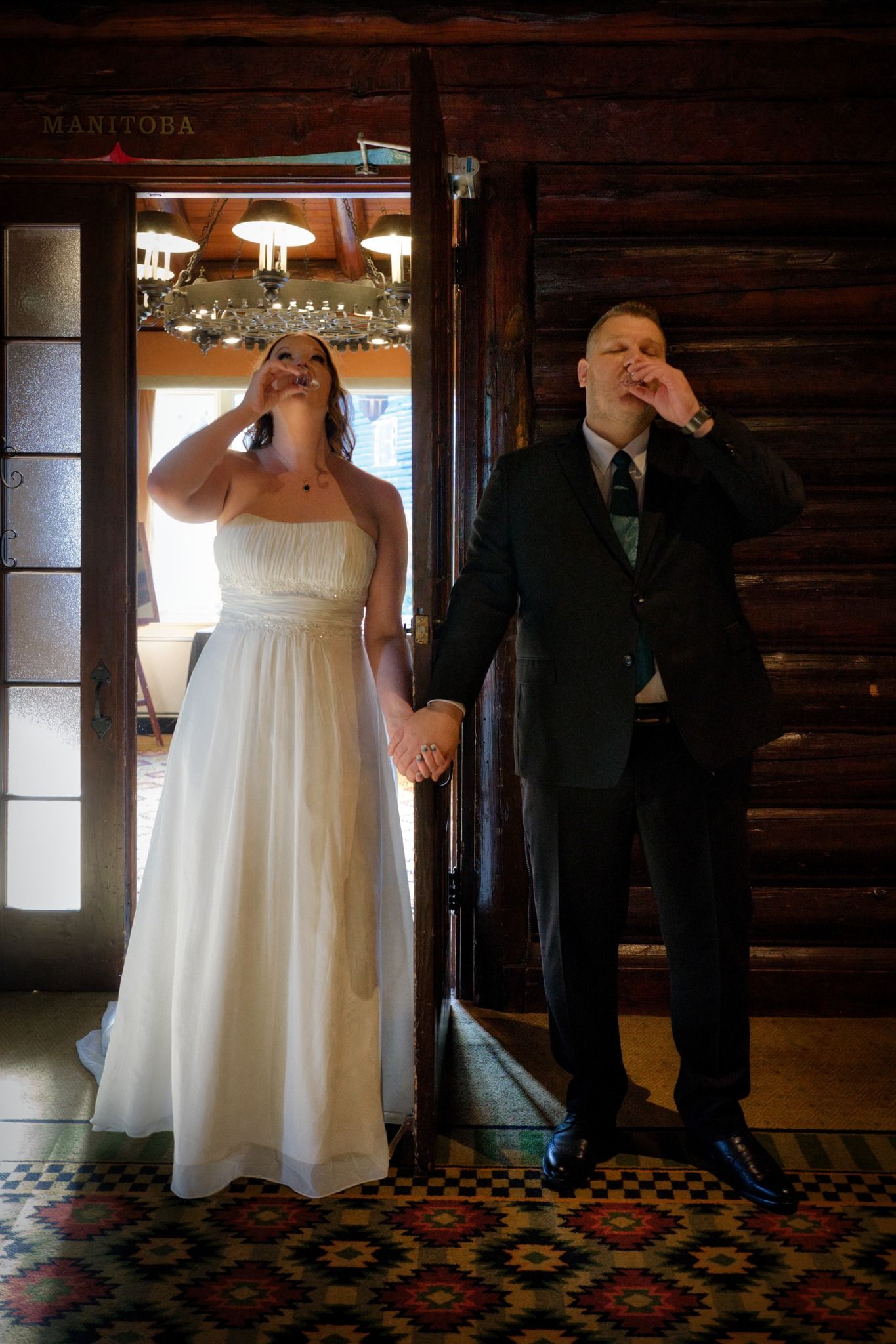 Wedding couple poses playfully inside rustic wooden barn with vintage decor.