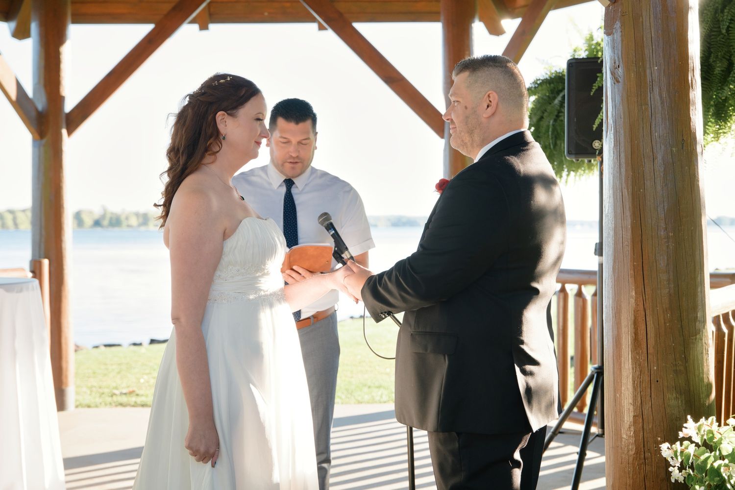 Wedding party gathers under a wooden outdoor pavilion during a celebration.