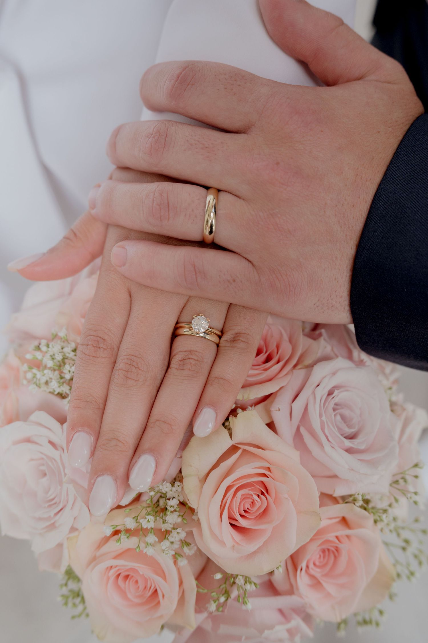 Close up of hands with wedding rings resting on delicate pink roses and baby's breath flowers.