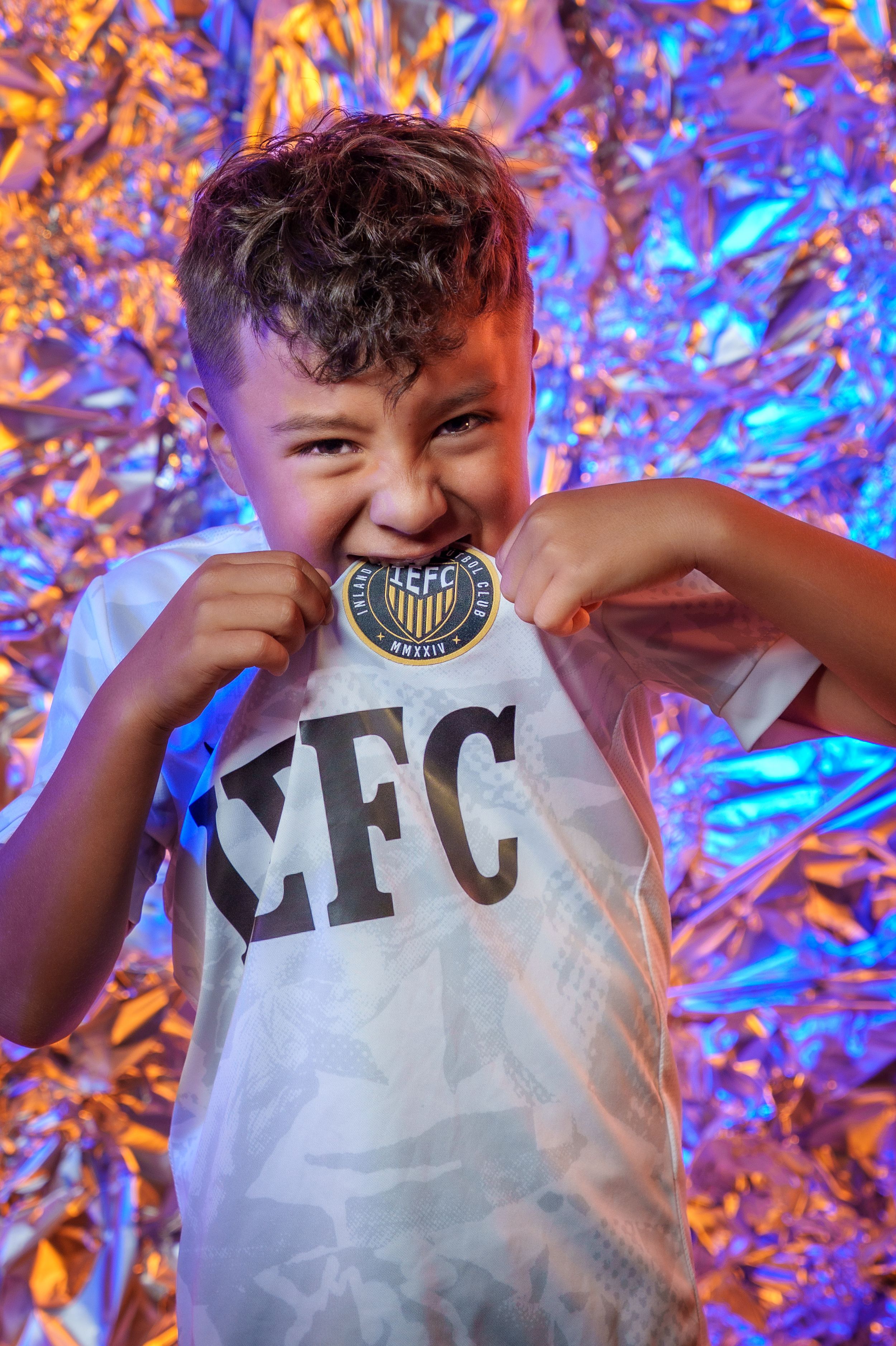 White sports jersey with IEFC logo displayed against vibrant metallic background.