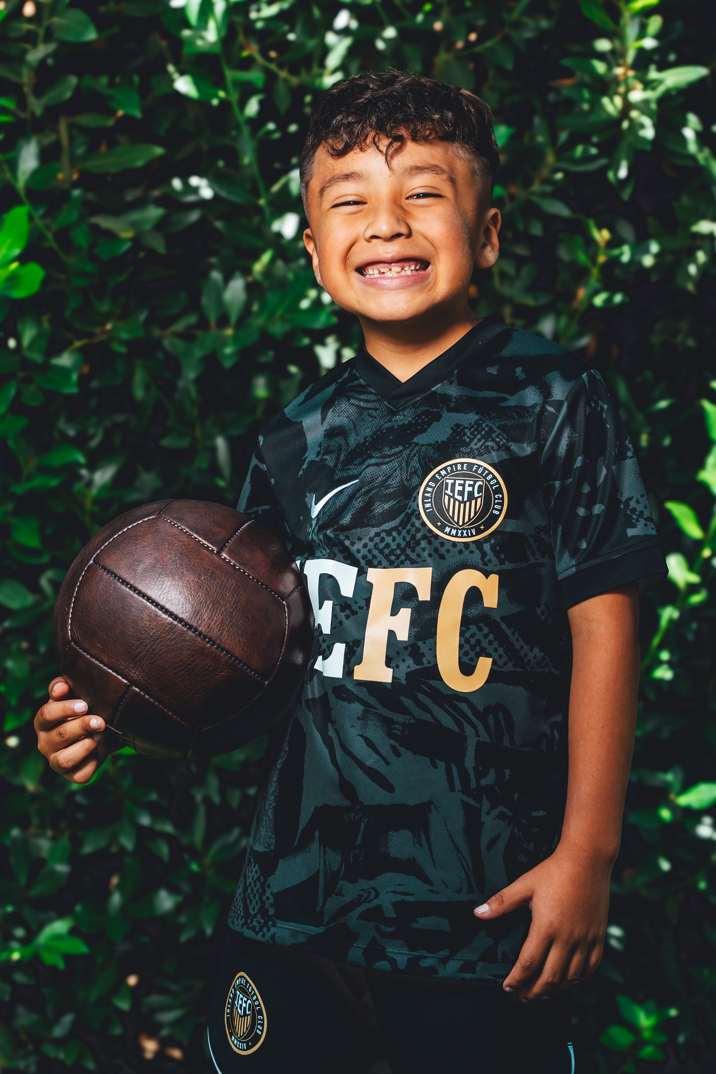 Black sports jersey with football prop photographed in natural outdoor setting with foliage.