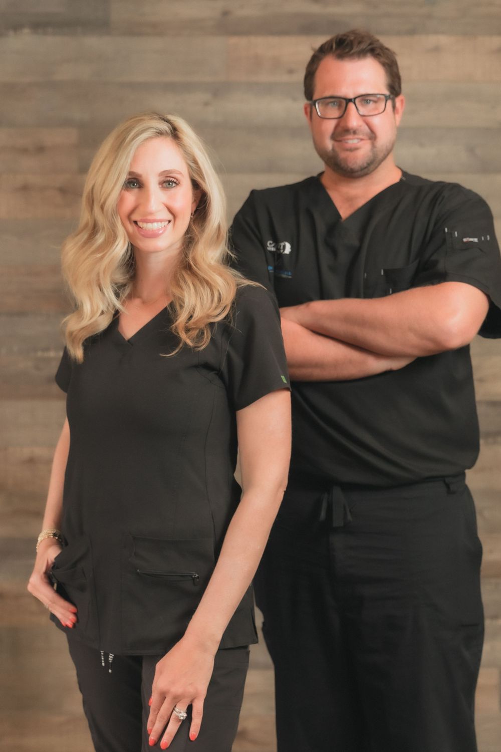 Professional team photo of two healthcare workers in black scrubs against wooden wall background. Mika Larson Photography.