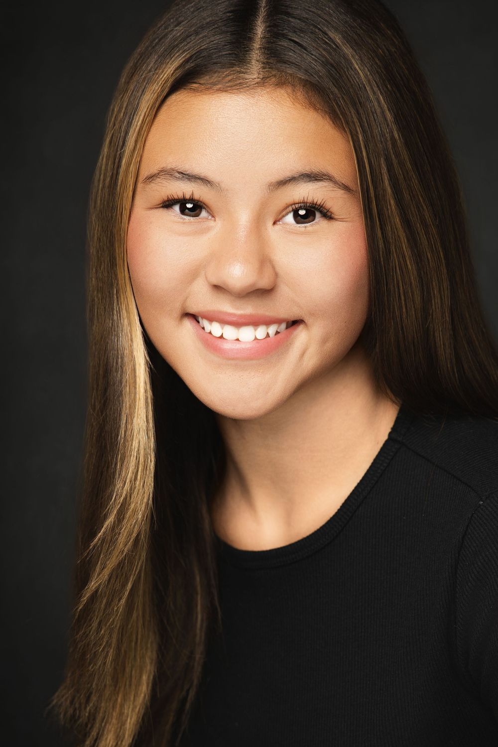 Professional portrait photo against dark background showing bright genuine smile and long straight brown hair.