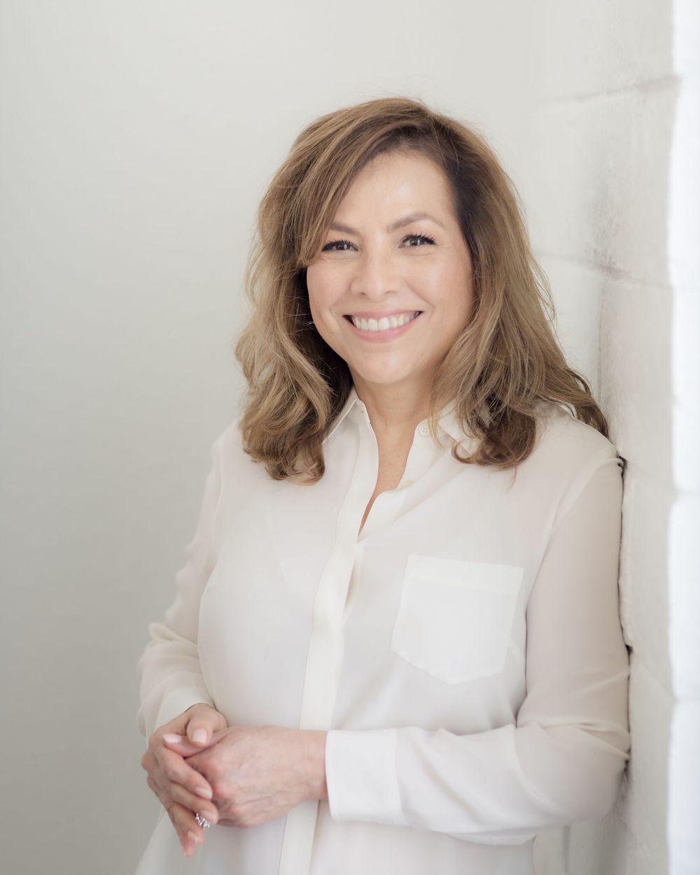 Professional headshot of person in white blouse smiling warmly against light background. Mika Larson Photography.