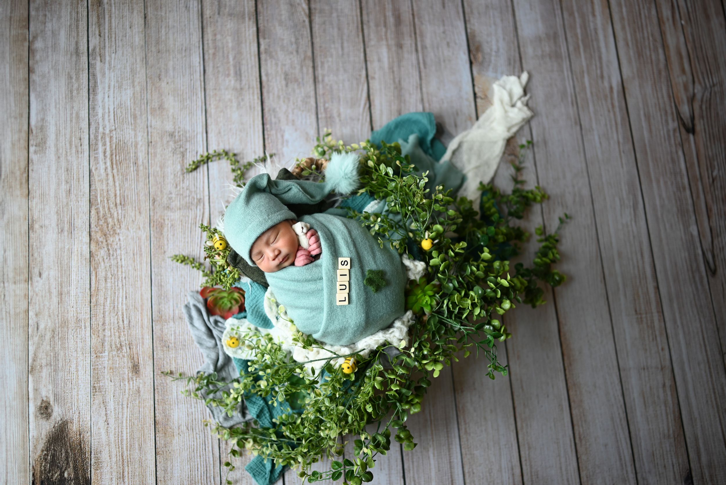 A decorative blue pumpkin nestled in greenery against a rustic wooden backdrop creates a whimsical fall display.