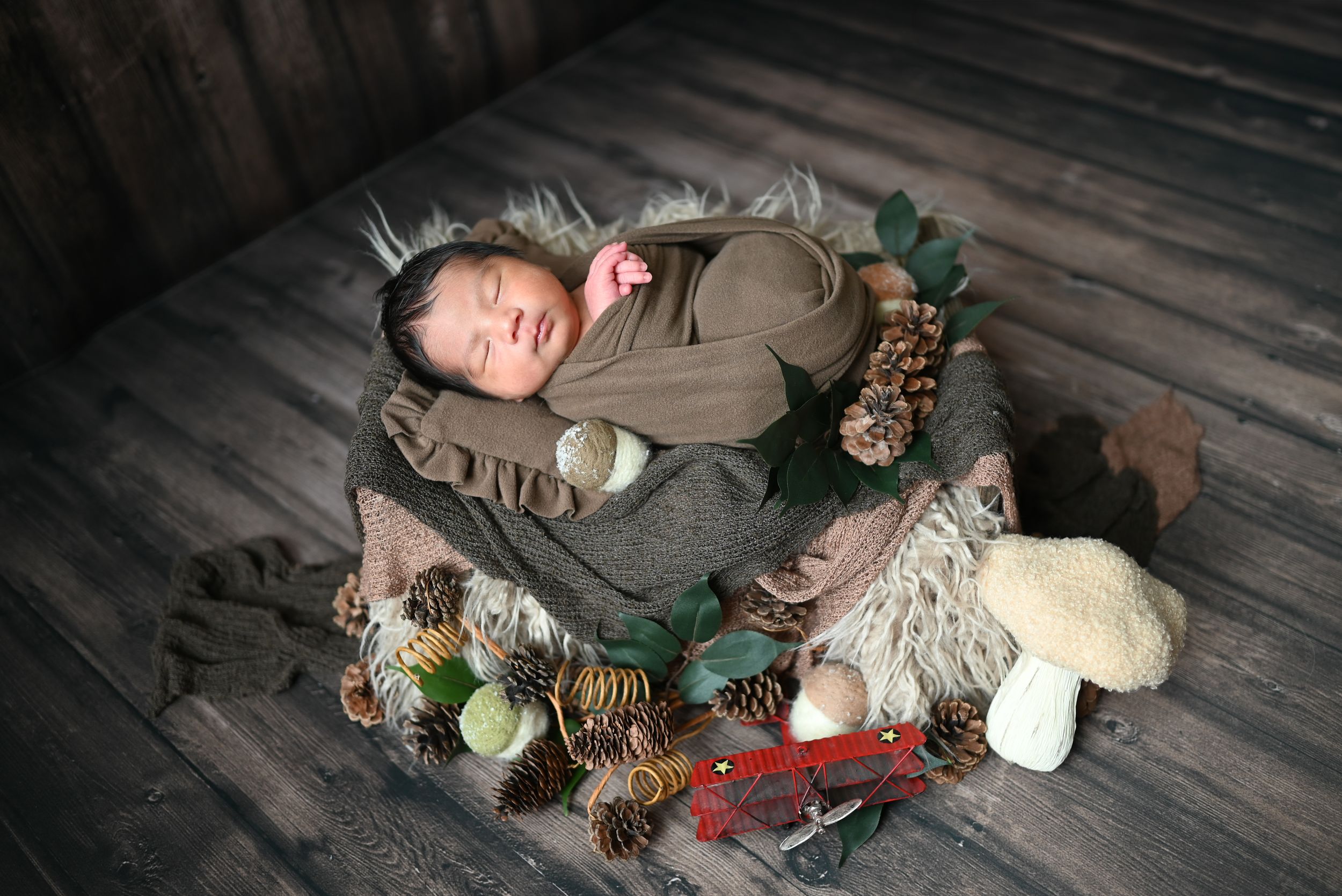 A sleeping baby lies on gray bedding surrounded by plush toys and stuffed animals in a wooden crib.
