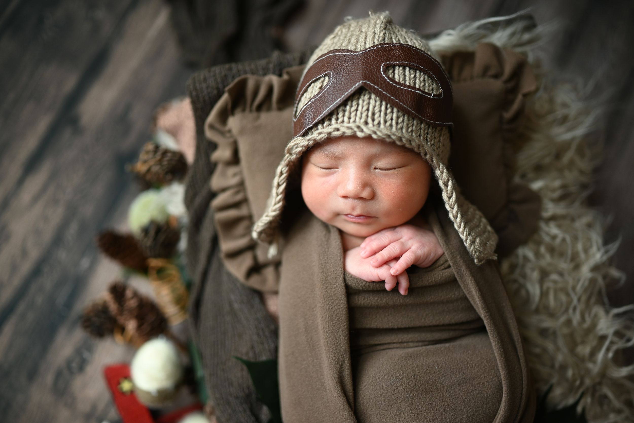 Newborn baby wearing a brown knit beanie lying on soft brown blanket during professional photo session in studio.