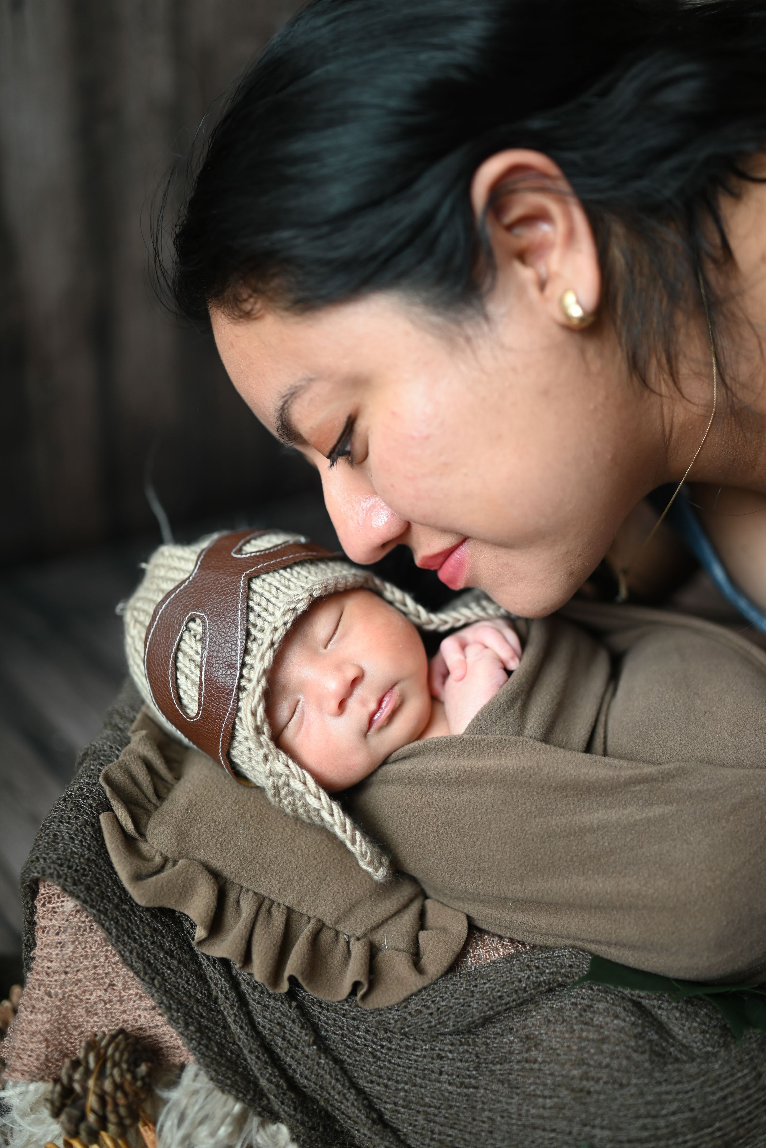 A tender moment captured between a mother and sleeping newborn baby wearing a knit bonnet.