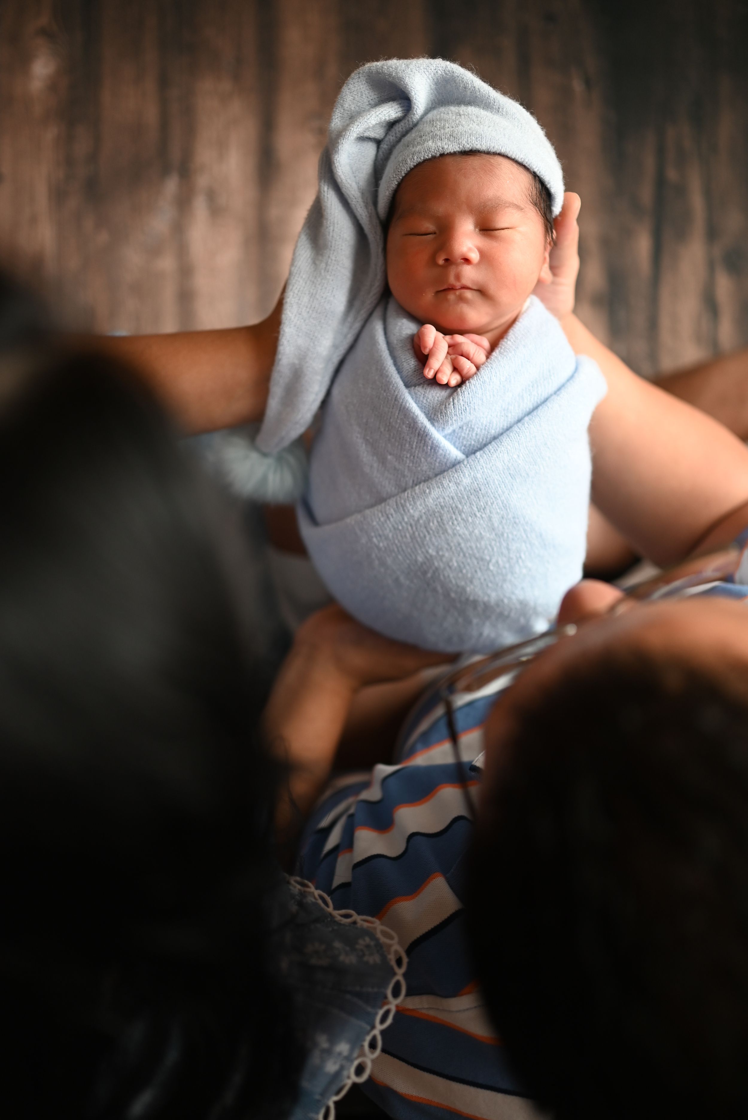 A sleeping newborn baby wrapped in soft gray swaddle and matching hat rests peacefully in natural lighting.